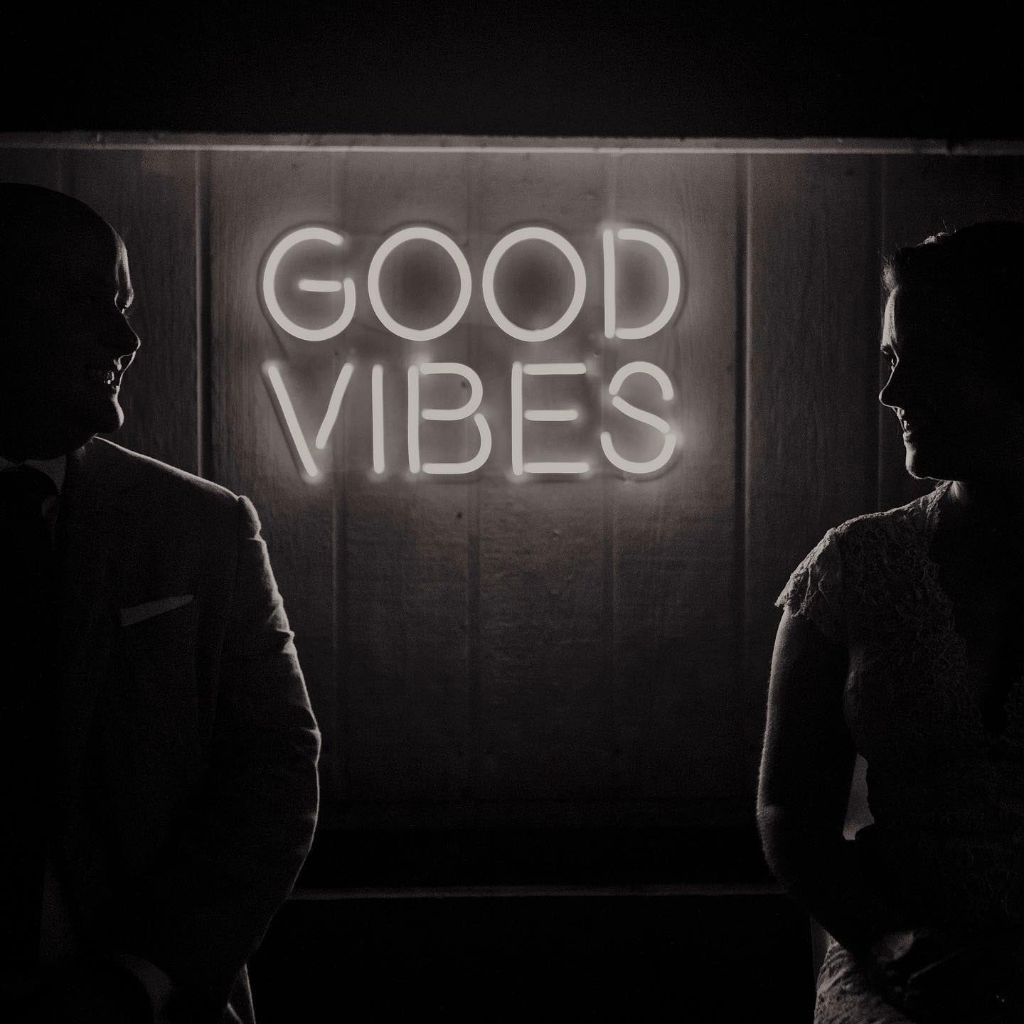 A silhouette of a couple standing next to an LED sign saying good vibes