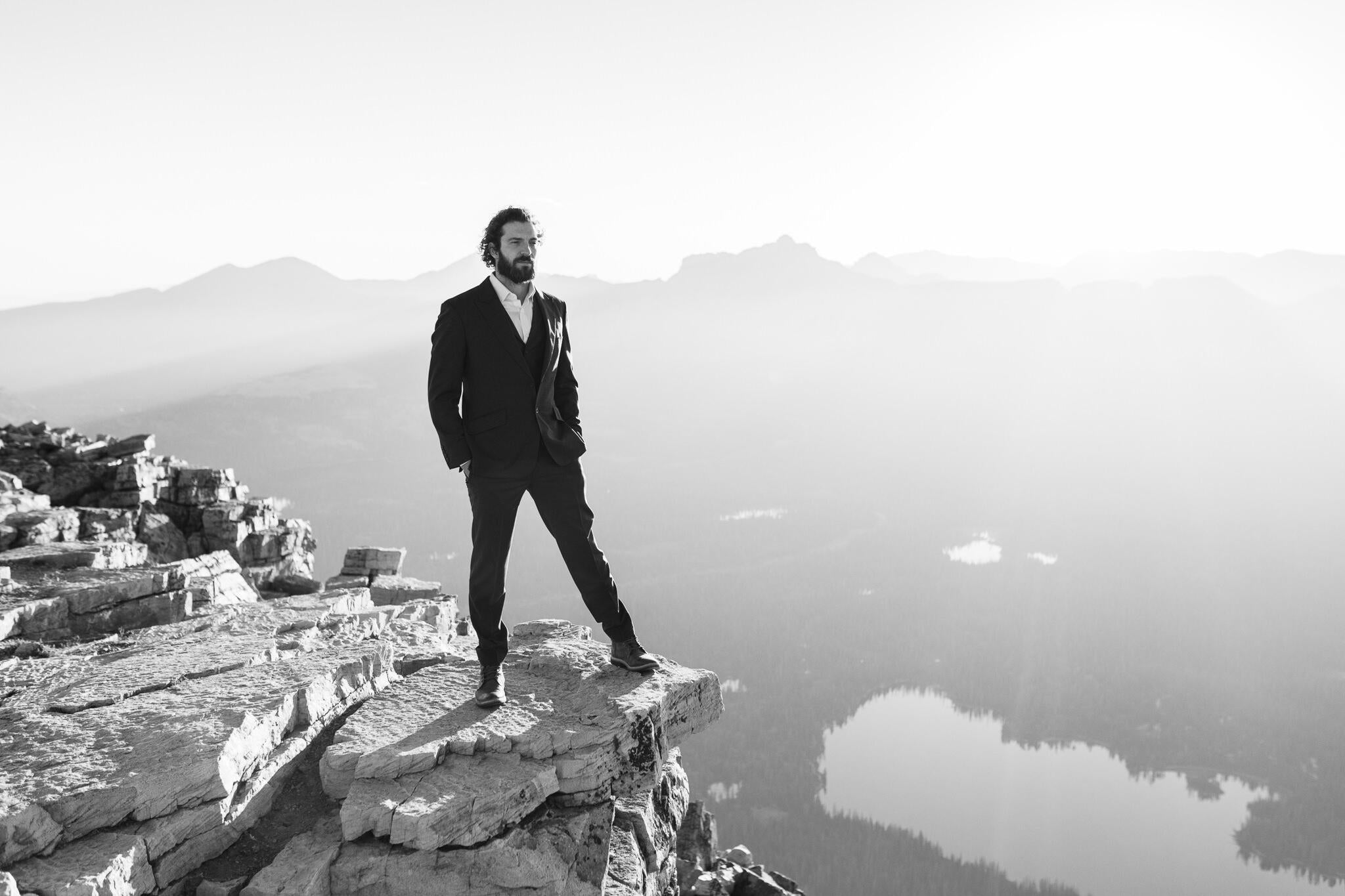 groom standing on edge of mountain in black and white