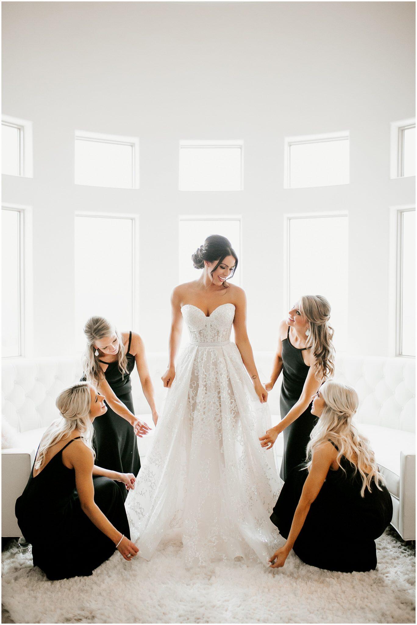 bride standing in getting ready room with bridesmaids all around her