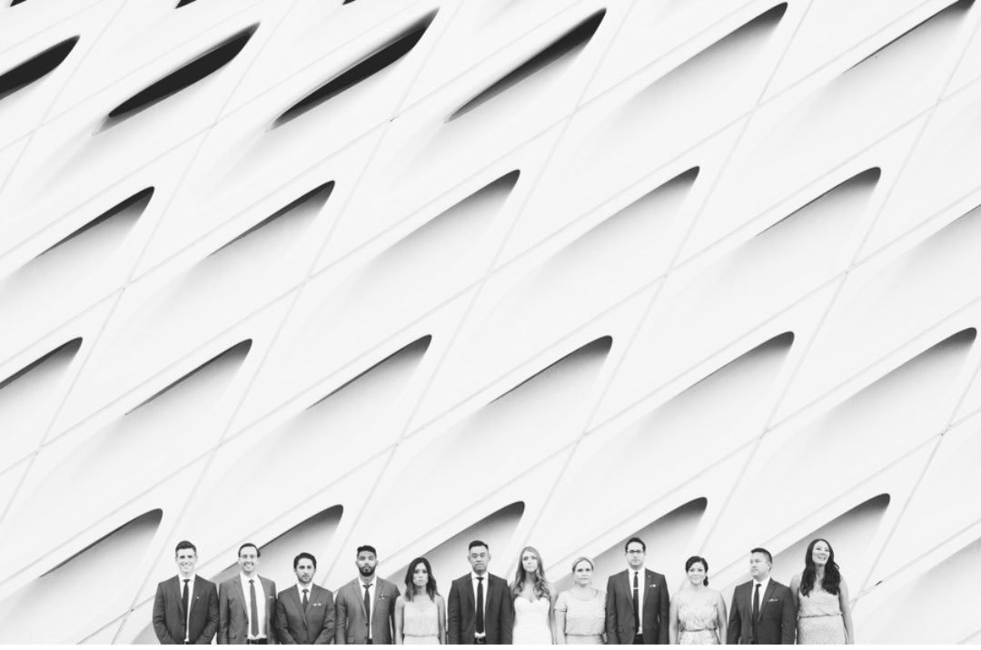 Black and white image of a bride and groom posing with the groomsmen and bridesmaids in front of a uniquely designed wall 