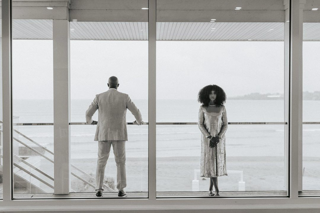 a bride and a groom standing in front of a large window facing opposite side