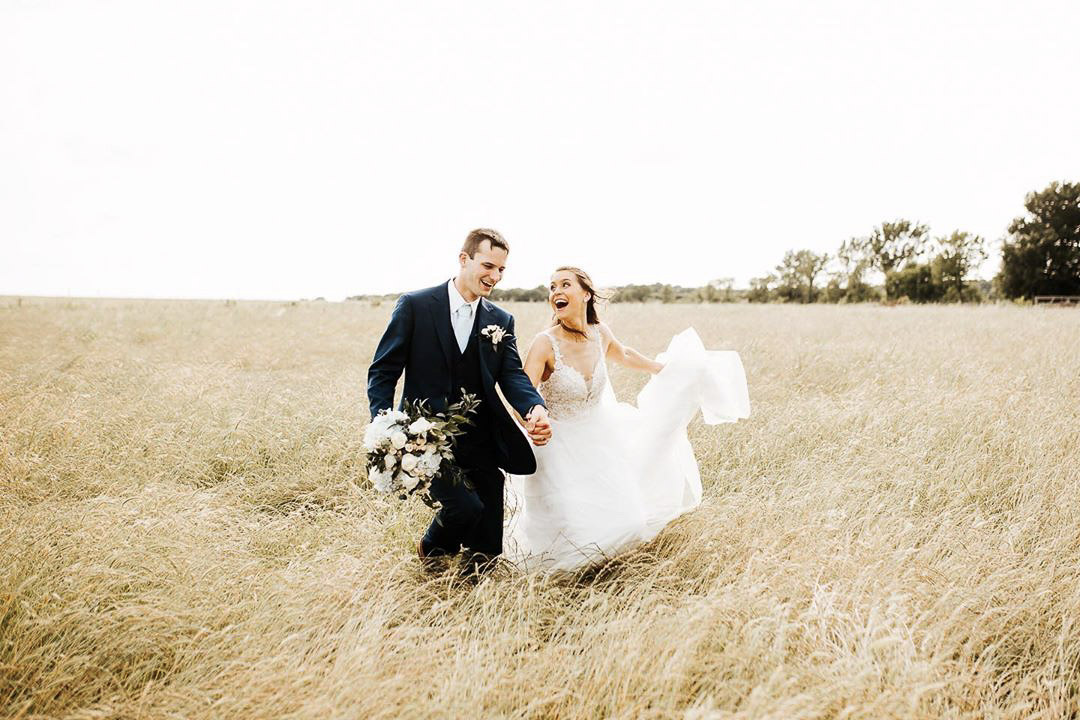 a wedding couple running through the hay field in their wedding attire