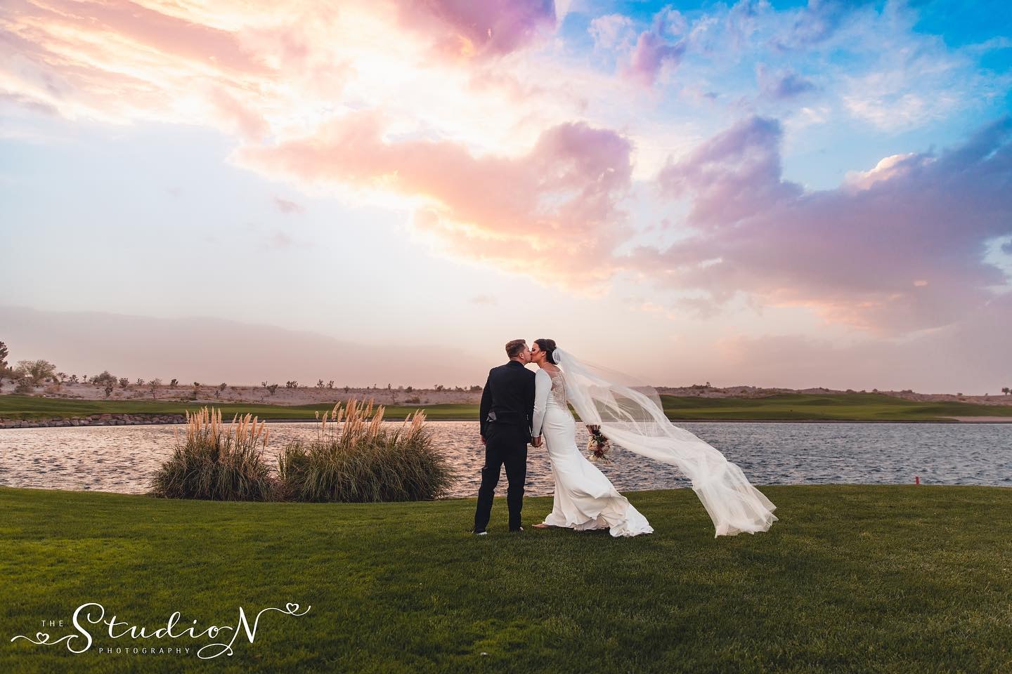 a newly wed couple kissing beside a beautiful lake in their bridal attire