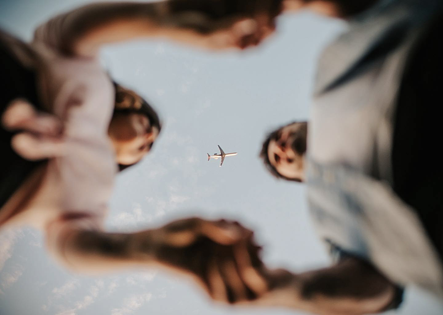 a moles eye view of a off focus couple holding hands while a plane is flying above them