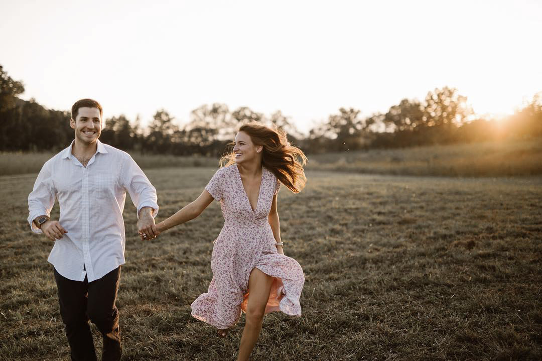 a couple running through a meadow while the sun is running behind them
