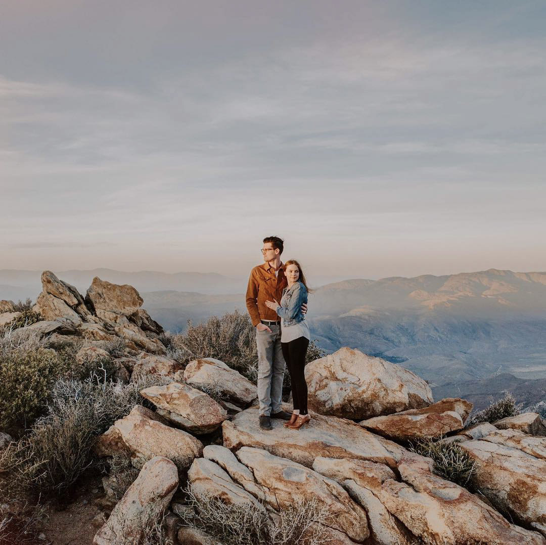 a couple standing on the top of a rocky mountain with a beautiful view