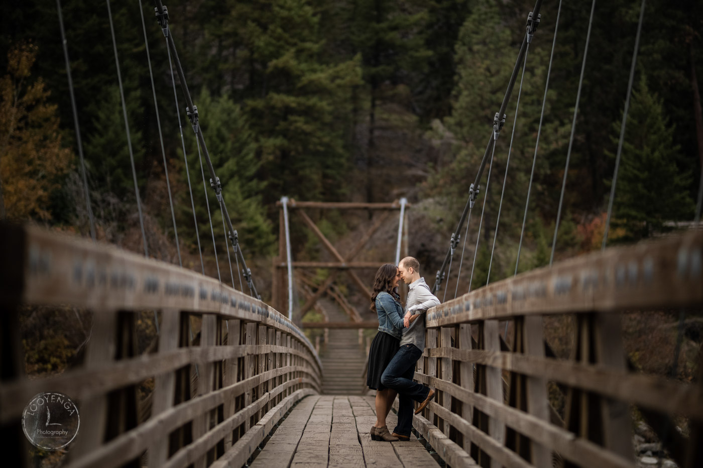 a wedding couple standing closely and posing on a hanging bridge