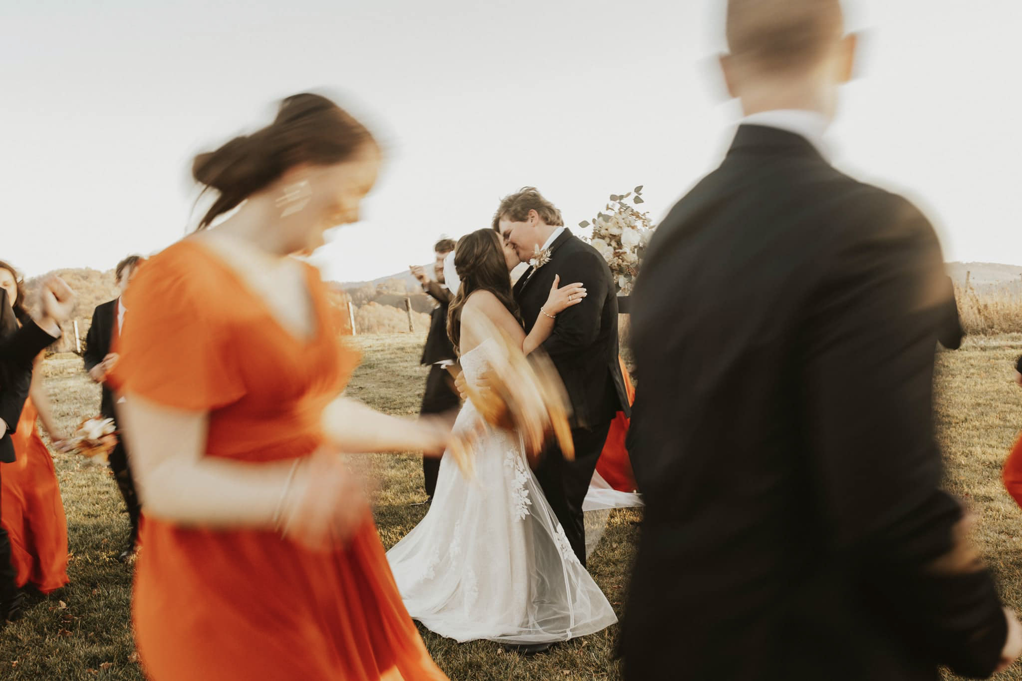a wedding couple kissing while the groomsmen and the bridesmaids are dancing surrounding them