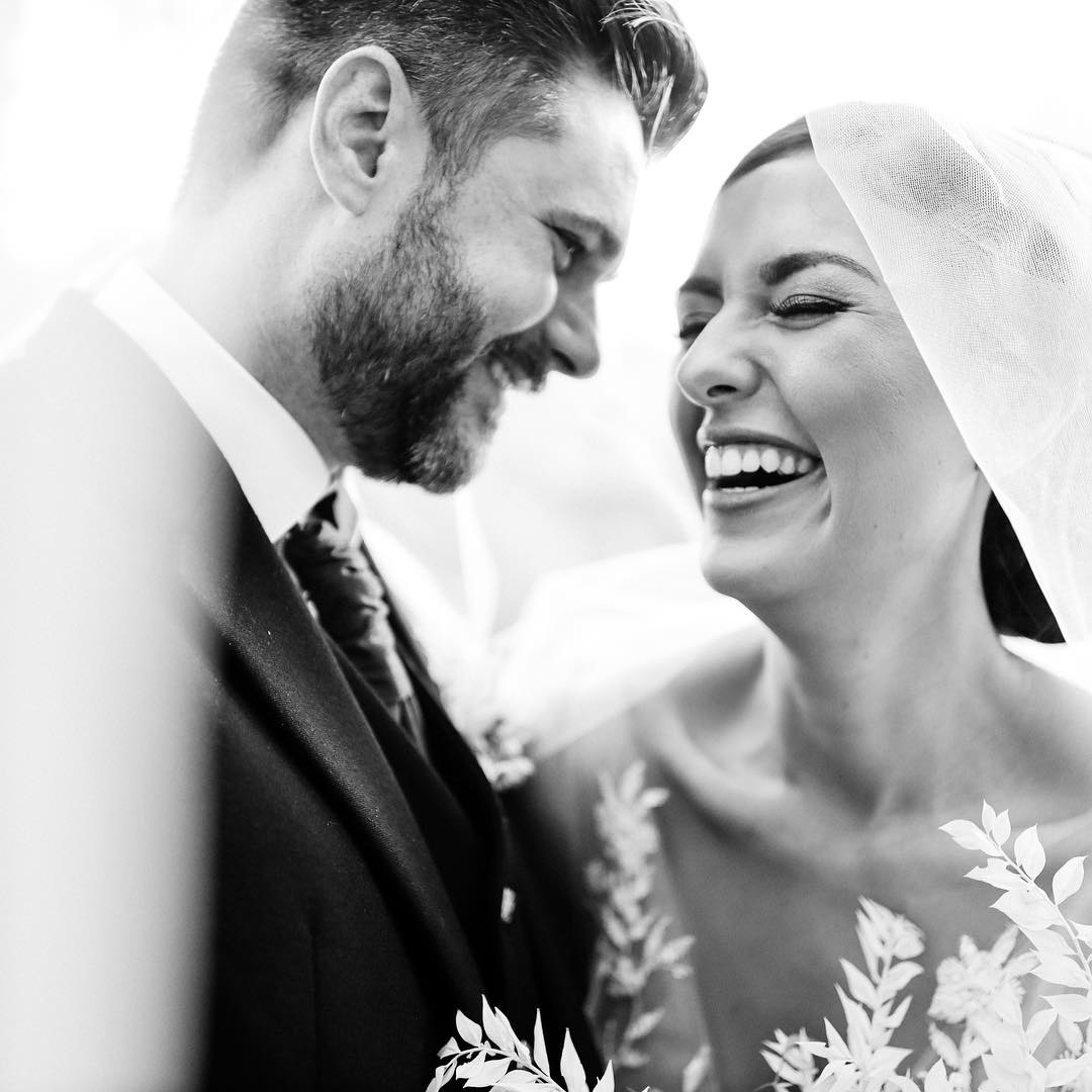 a black and white portrait of a wedding couple laughing under the wedding veil