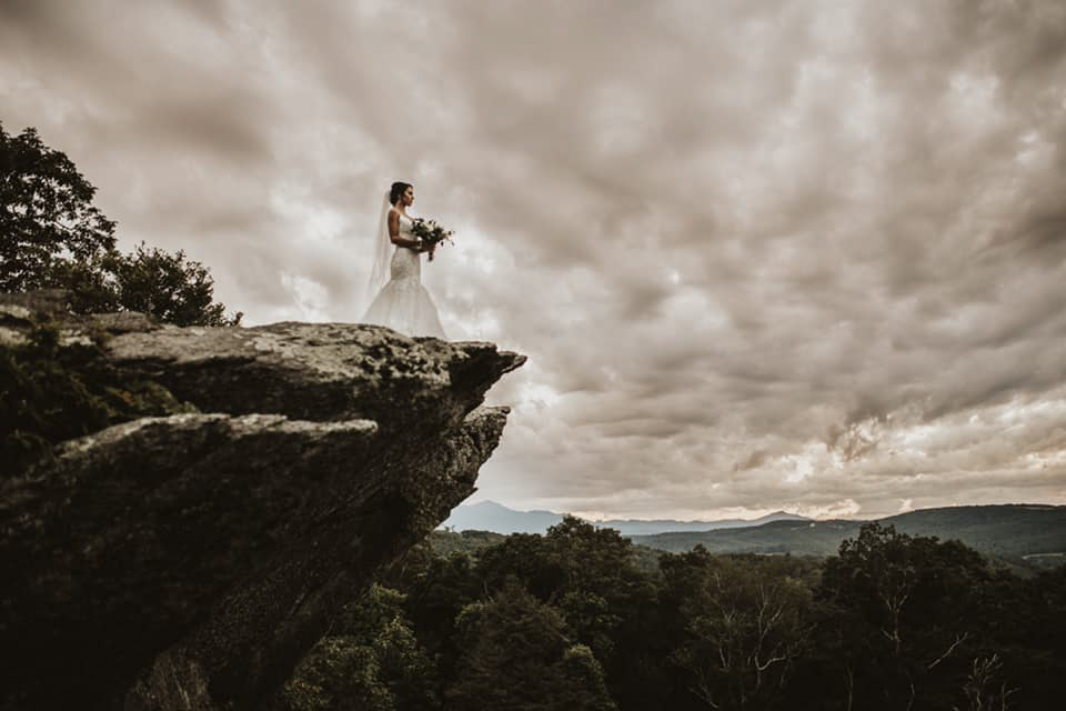 a bride carrying her wedding bouquet standing on the edge of a rocky cliff
