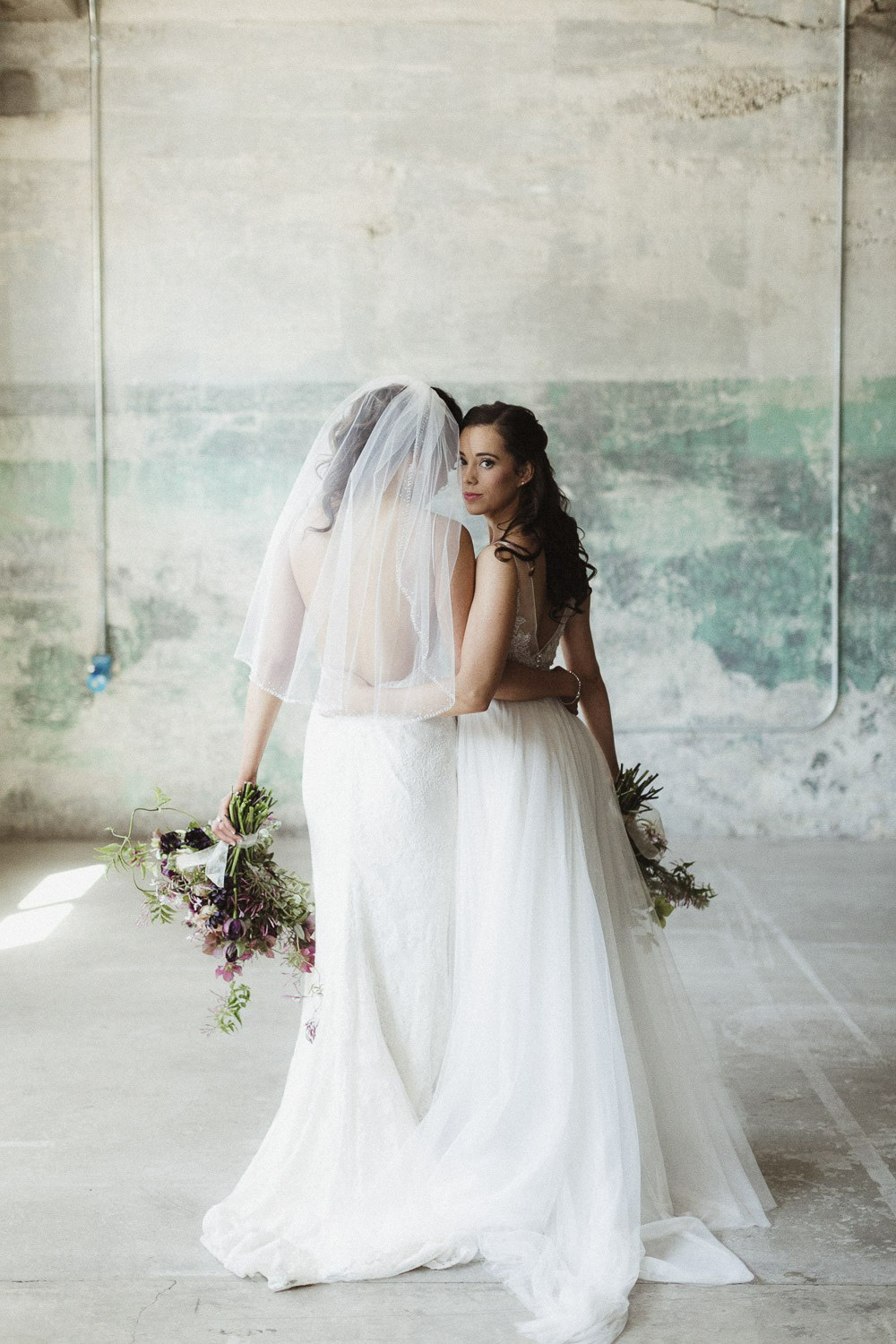 two brides in their wedding dresses posing holding their wedding bouquets
