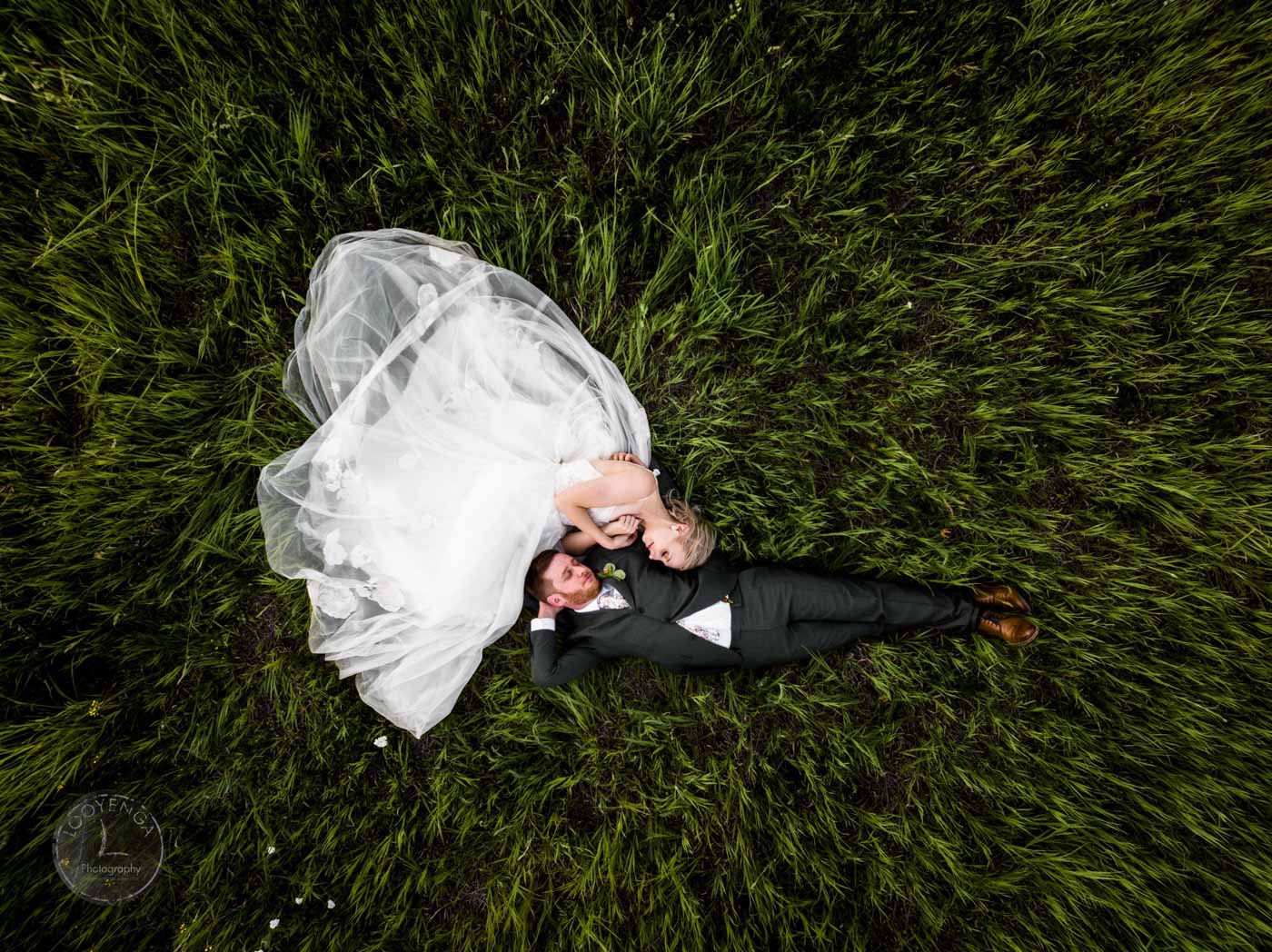 a top down shot of a wedding couple lying down on grass in their wedding attire