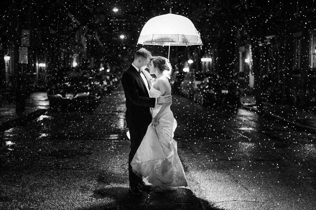 a black and white image of a couple standing in the middle of the road in rain holding an umbrella