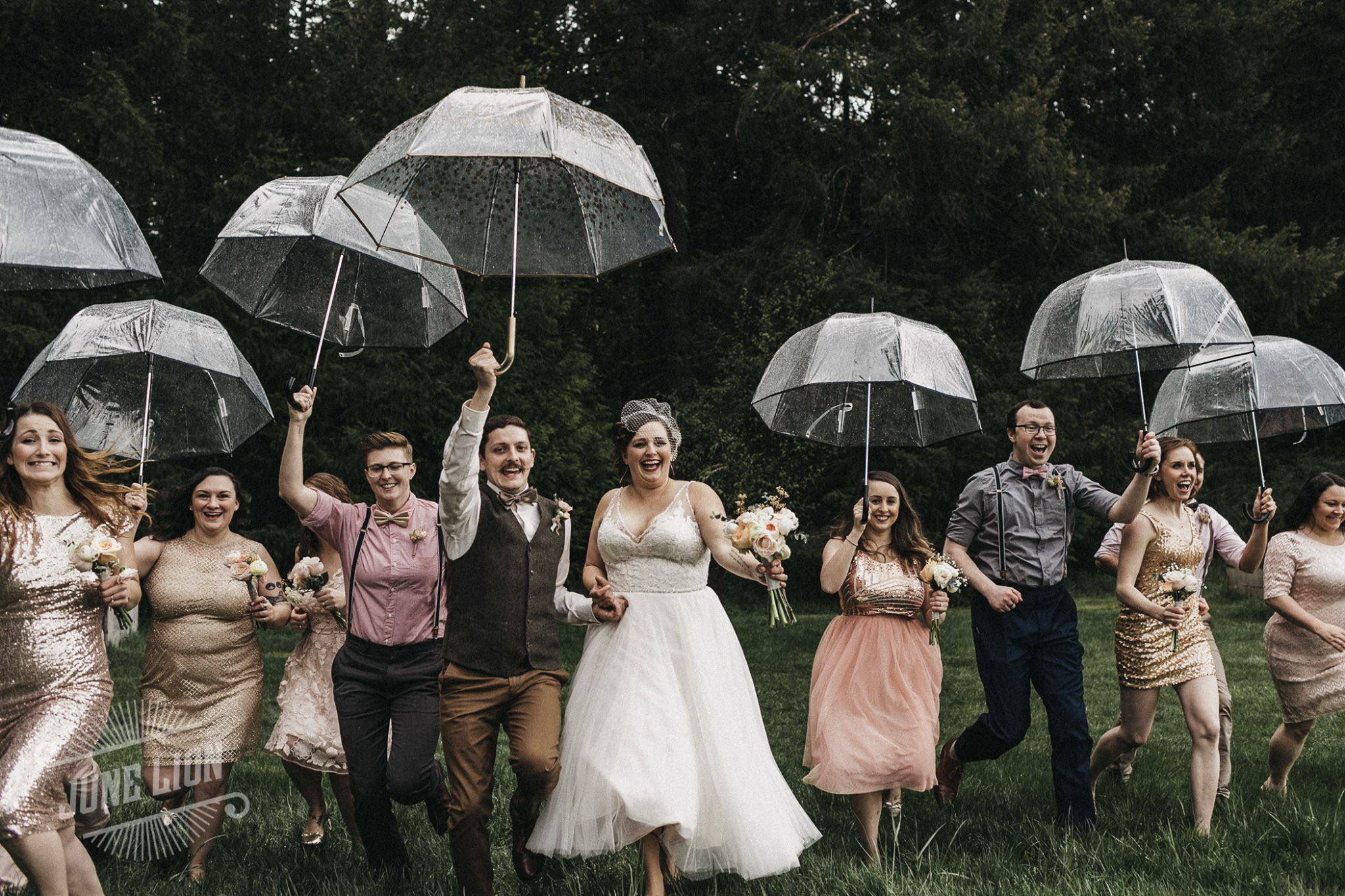 a wedding couple and the bridesmaids and groomsmen running towards the camera holding umbrellas