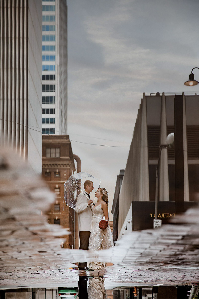 the reflection of a couple in wedding attire on a street puddle