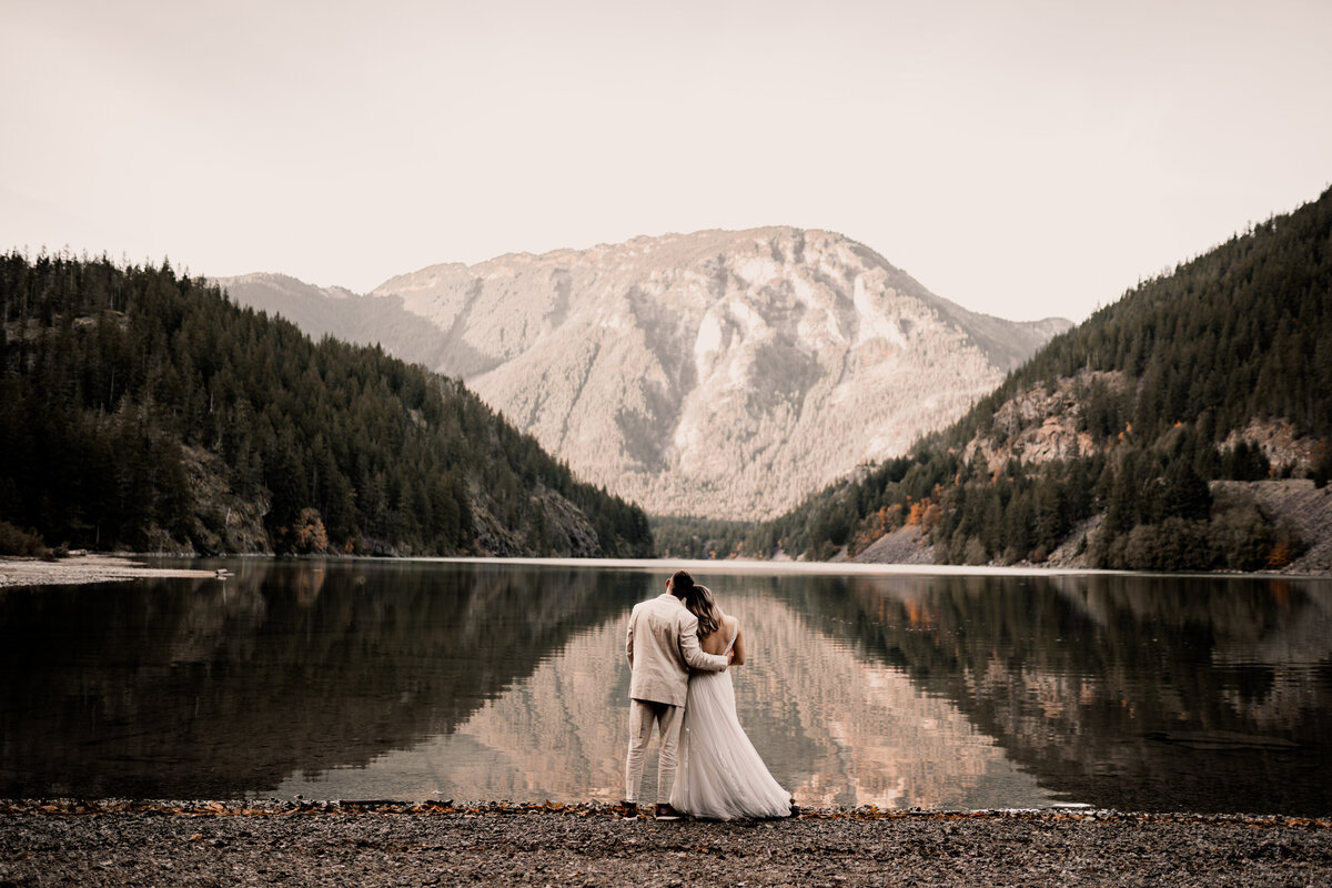a couple standing facing a beautiful lake surrounded by hills reflections in wedding photography