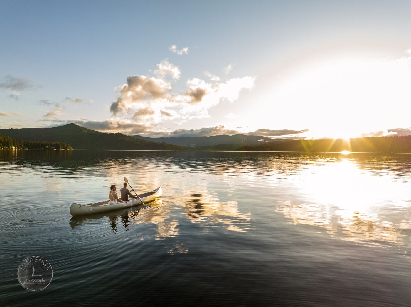 a couple sailing on a canoe on a lake towards a beautiful sunrise