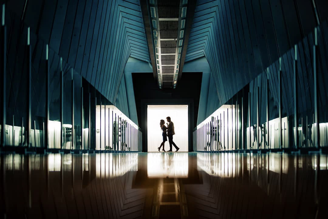 a couple posing at the end of a hallway with multiple reflections on the wall