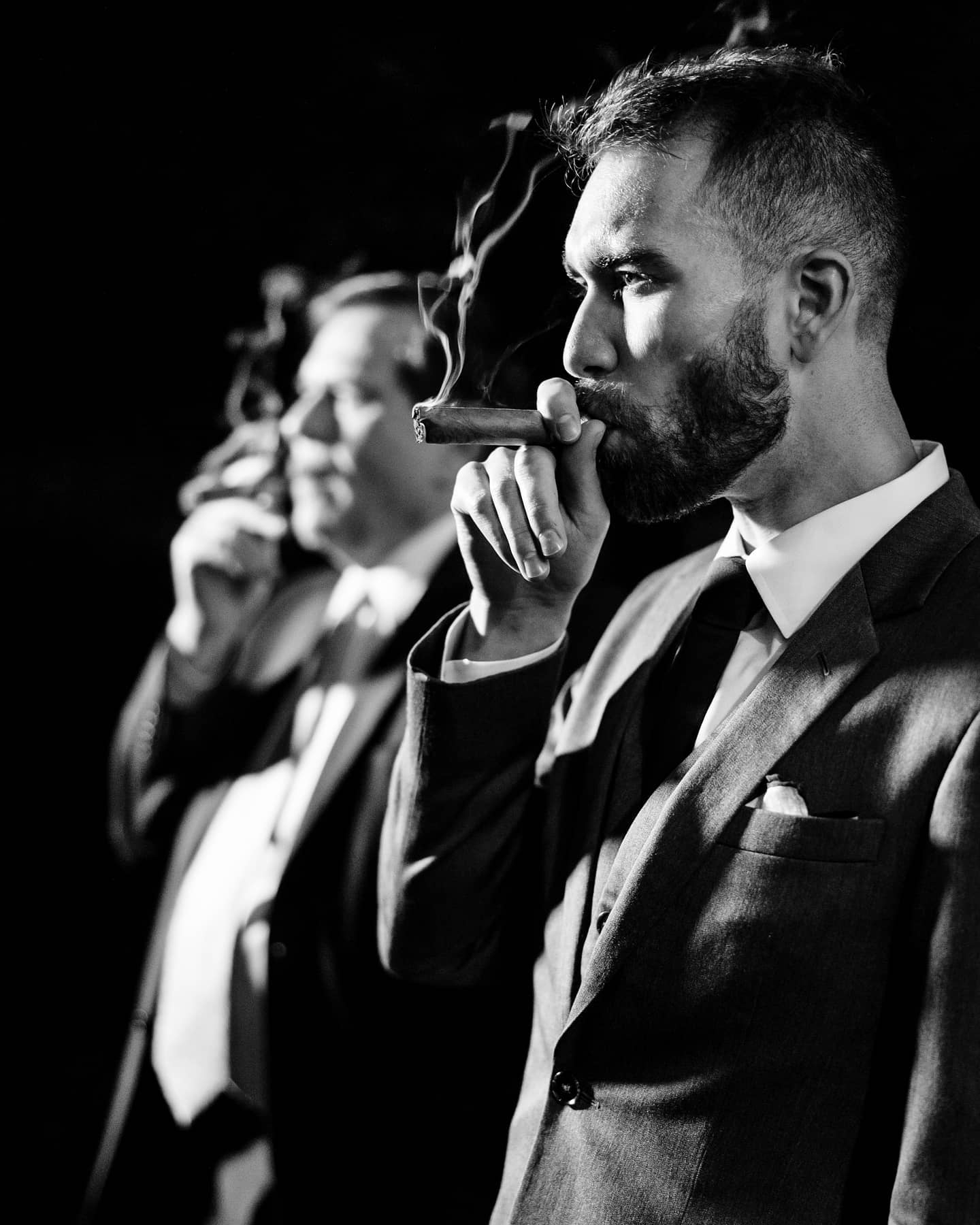 A monochrome portrait of a groom smoking a cigar