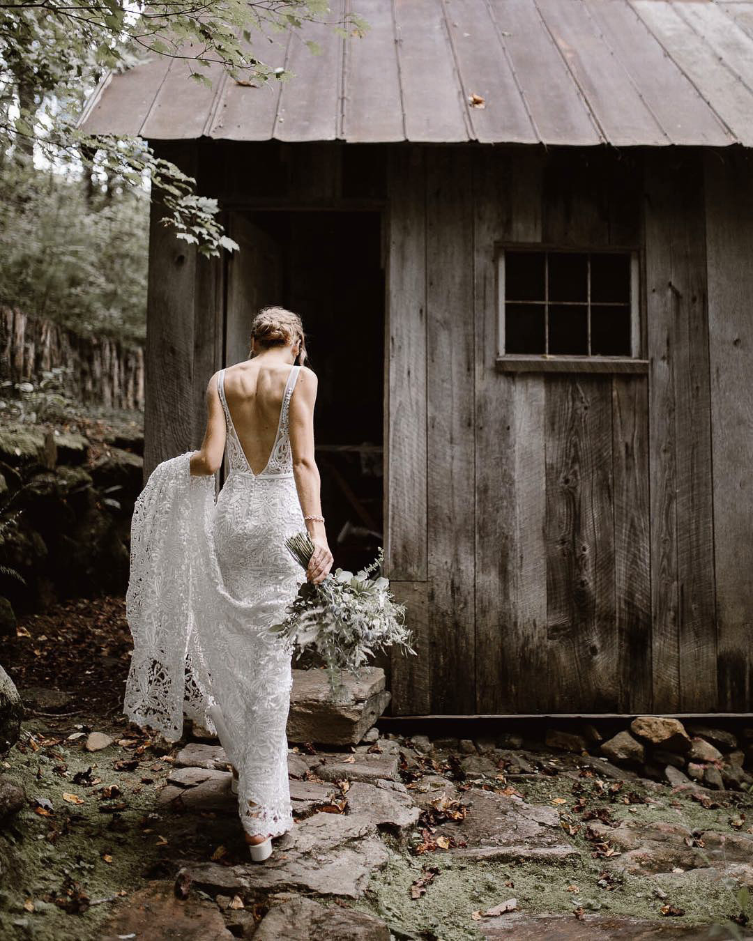 a bride in her wedding attire entering a wooden shack with her wedding bouquet