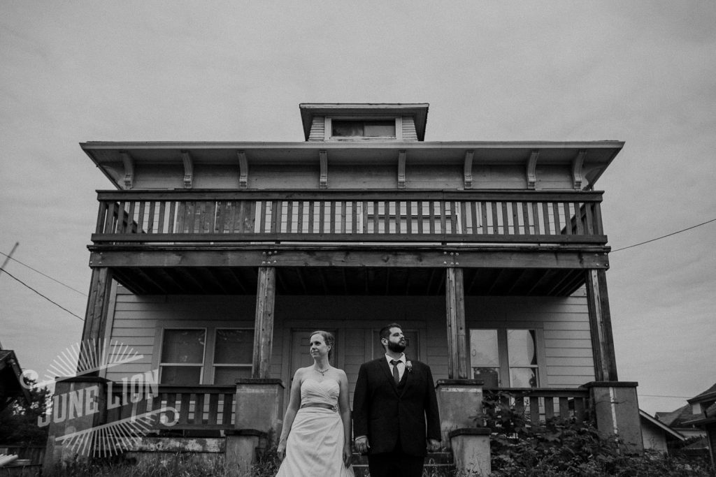 a black and white shot of a wedding couple standing side by side a wooden mansion