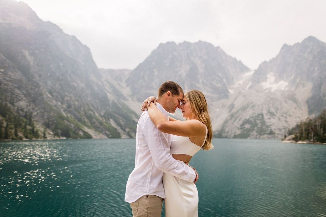 a couple closely embracing each other in front of a lake surrounded by mountains