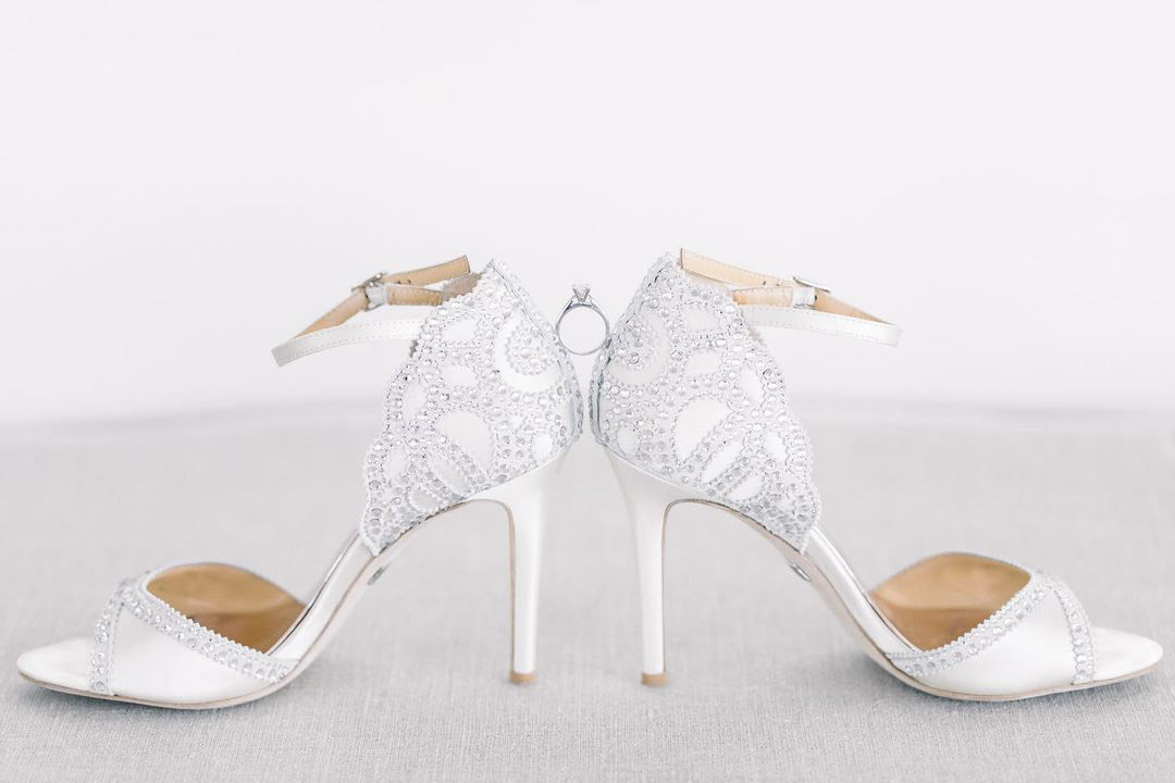 a wedding ring perfectly placed in between the two bridal shoes