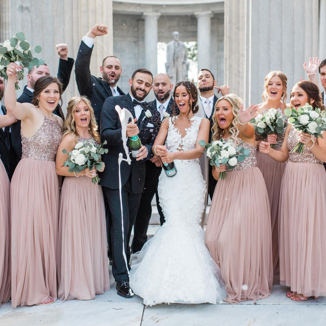 Bride and groom popping open the champagne bottle while being surrounded by bridesmaids and groomsmen