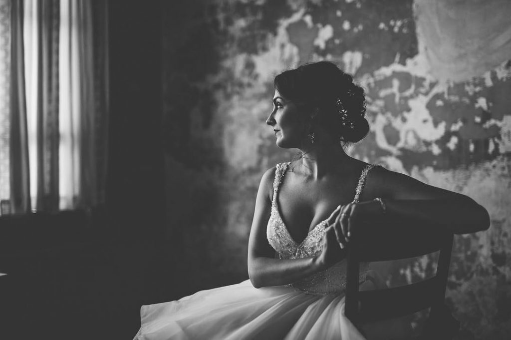 a black and white image of the wedding bride staring at a window 