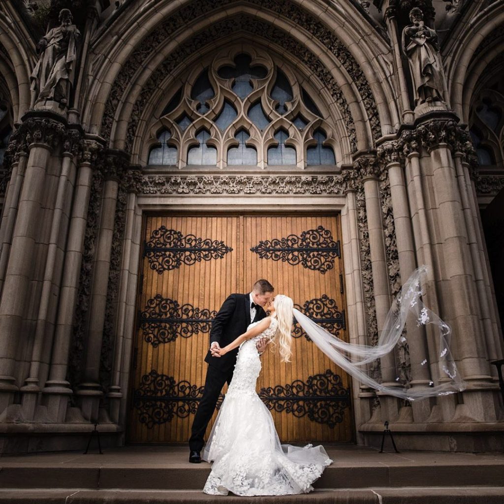 a bride and a groom kissing while the bride's veil is being blown by the wind