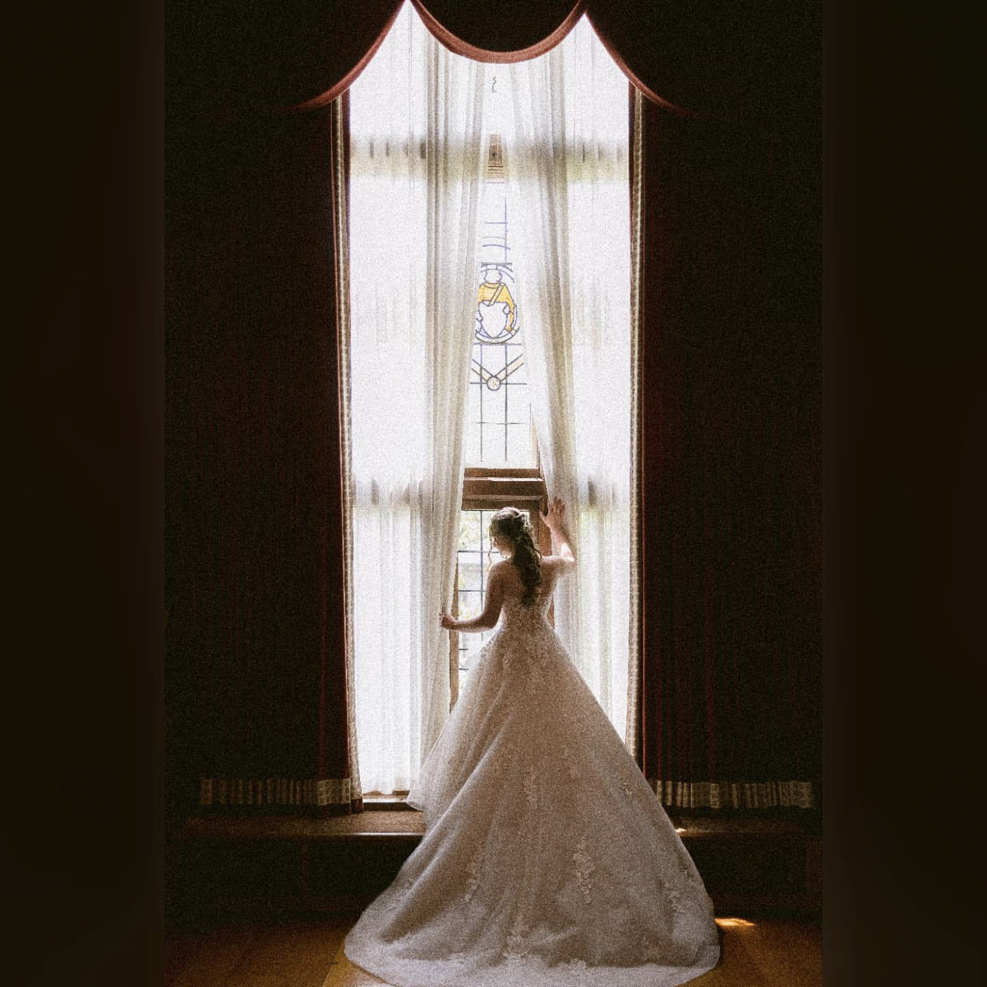 a wedding bride parting the large curtains of a dark room