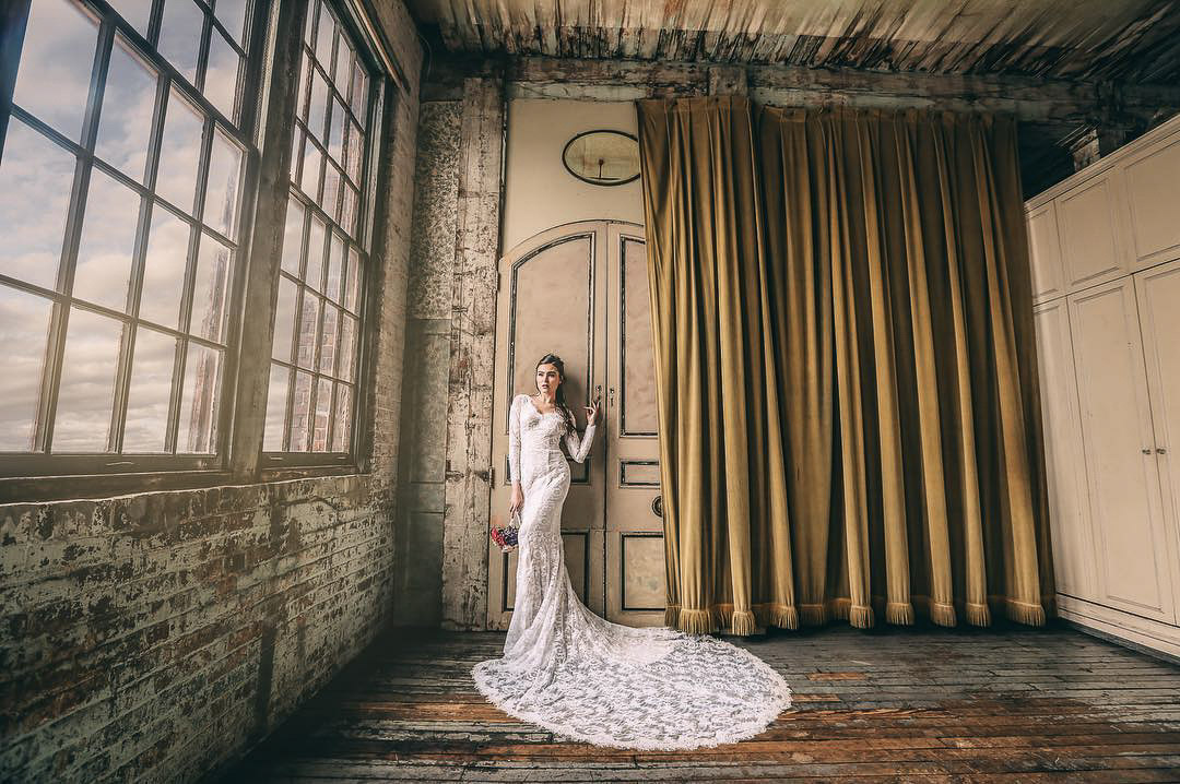 a bride posing in front of a large door and curtains while the sky is visible through the windows