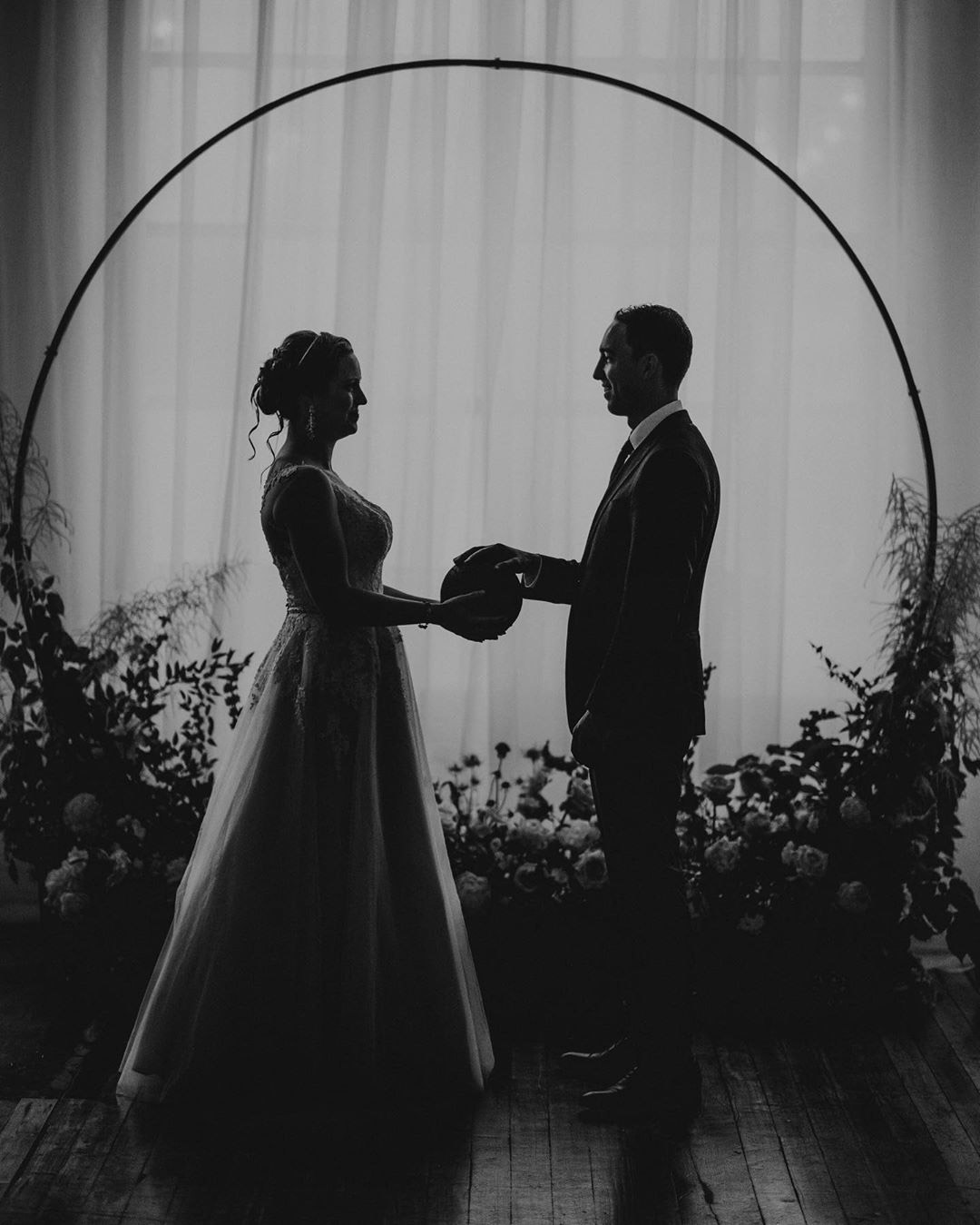 a silhouette of a wedding couple holding hands standing in front of the wedding arch